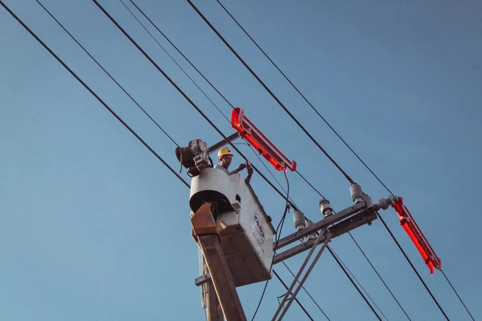 Electrician in a lift repairing overhead power lines on a clear day.